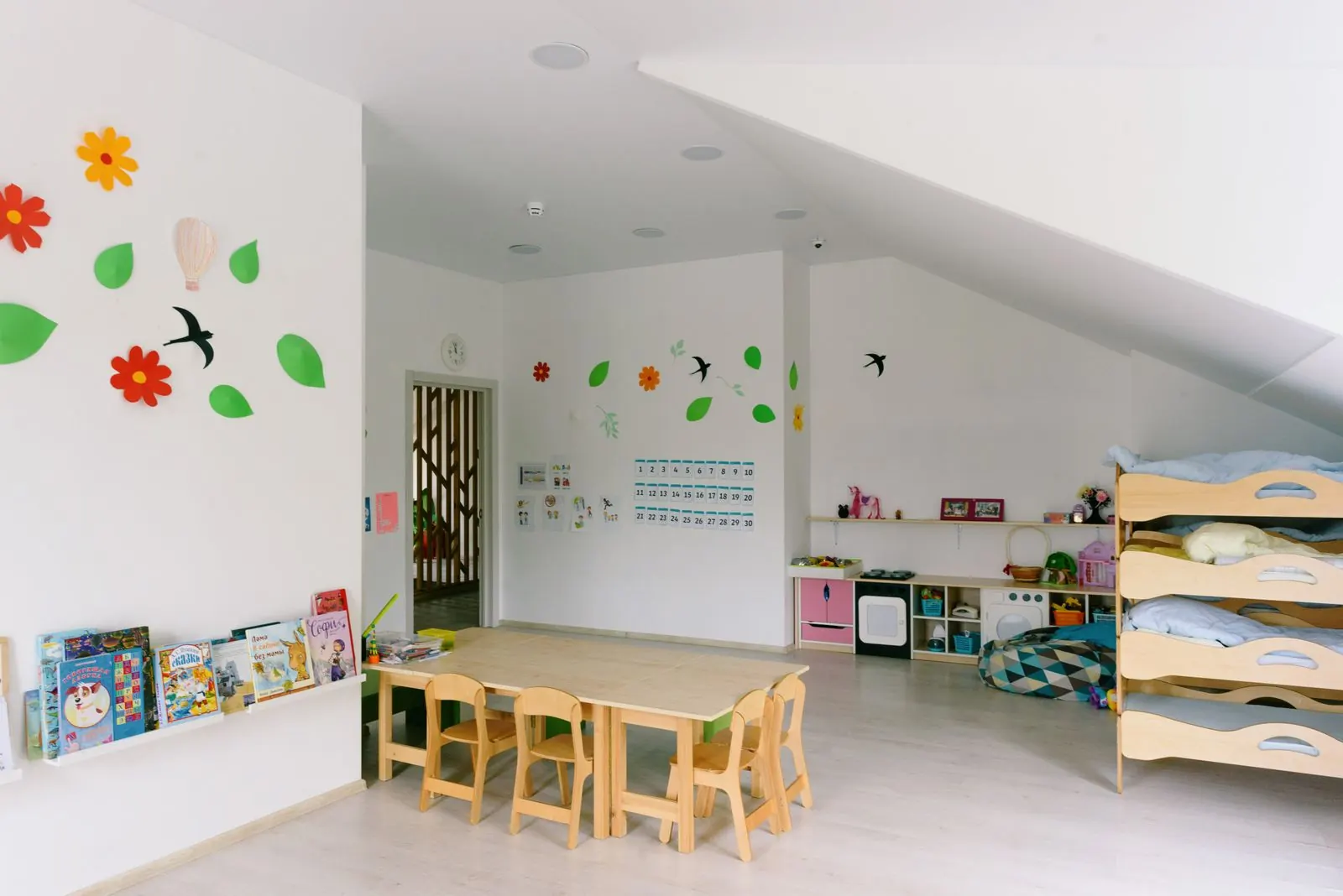 A childcare room with low tables and stacked toddler beds