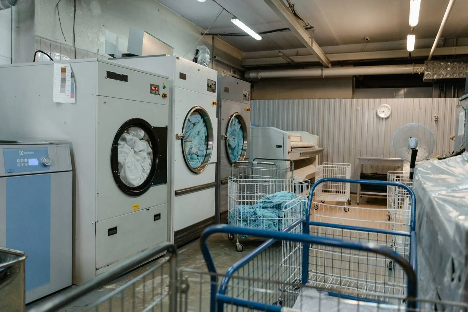 Commercial washers and linen carts in a clean, bright laundry room