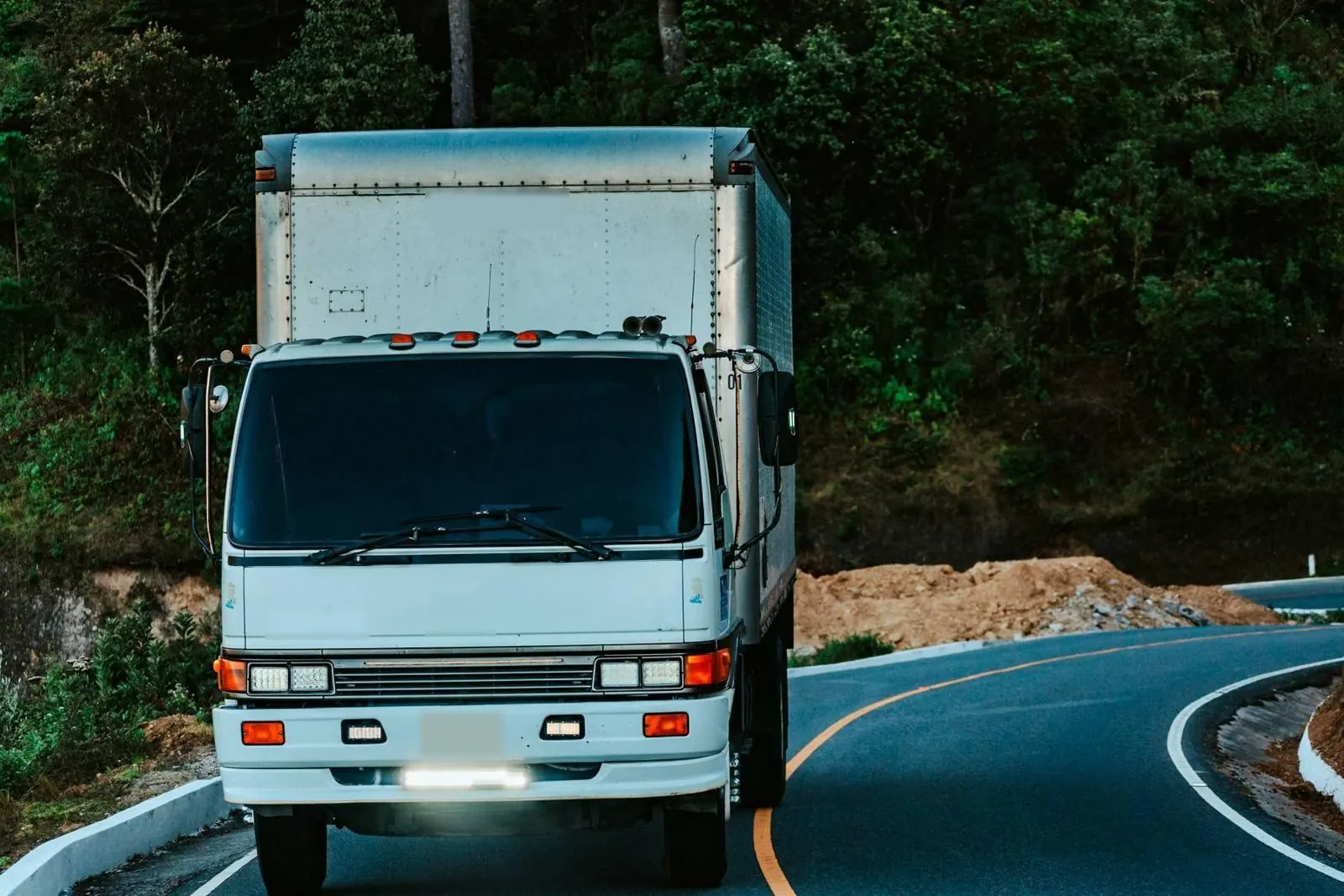 A white box delivery truck on a road through green hills