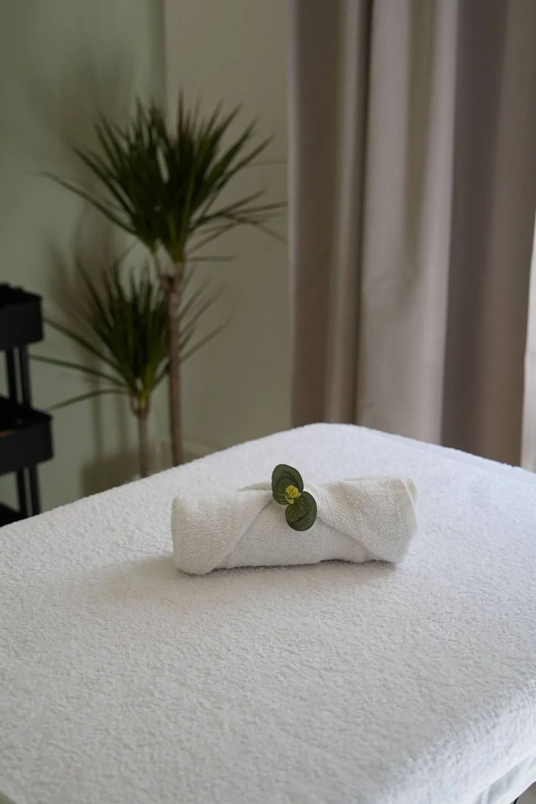 A spa treatment table dressed in white linens with a rolled towel