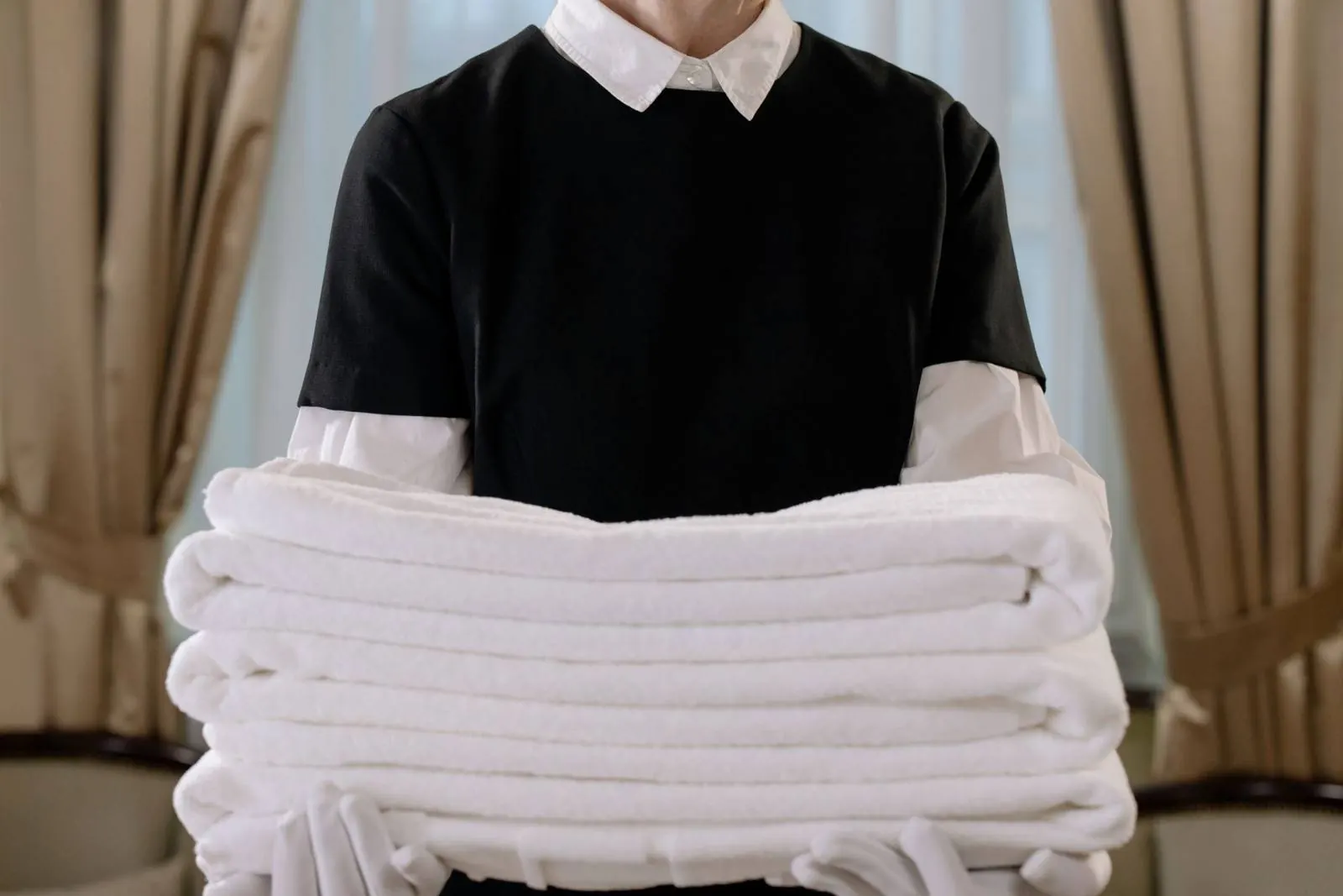 A housekeeper holding a tall stack of folded white towels